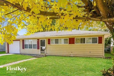 the front of a yellow house with a yard and a tree