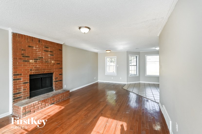 an empty living room with a brick fireplace and wooden floors