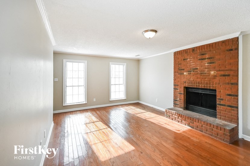 an empty living room with a brick fireplace and wooden floors