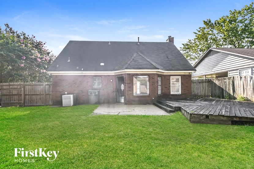 a small brick house with a backyard and a wooden deck