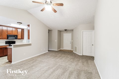 an empty living room with a ceiling fan and a kitchen