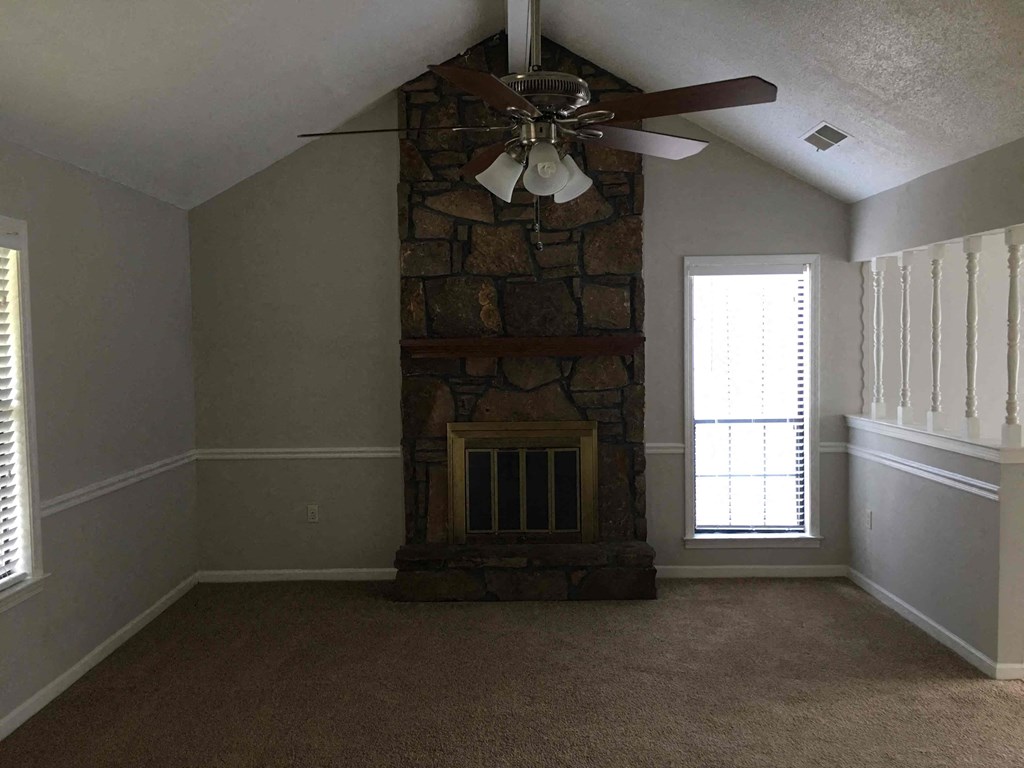 A room with a stone fireplace and a ceiling fan.