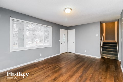 A spacious room with wooden floors and a staircase leading to another room.
