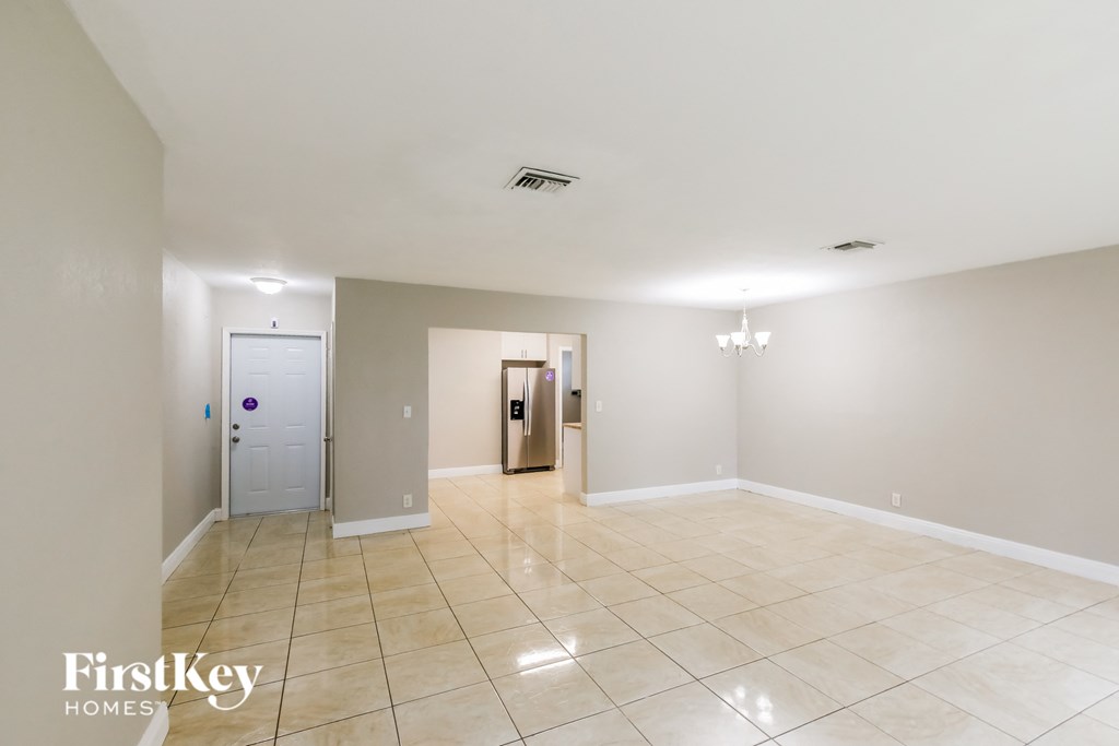 a empty living room with a tiled floor and a door to a hall way