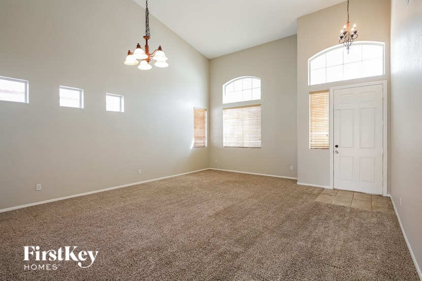 A spacious room with a carpeted floor, a chandelier, and a door at the end.