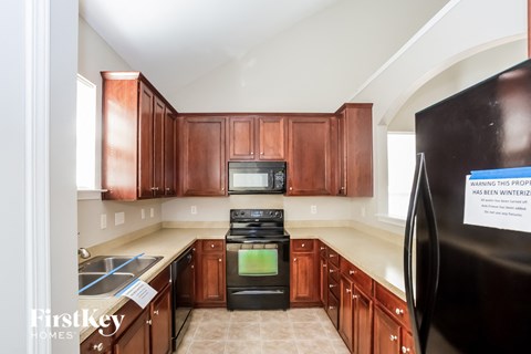 A kitchen with brown cabinets and a black refrigerator with a sign on it.
