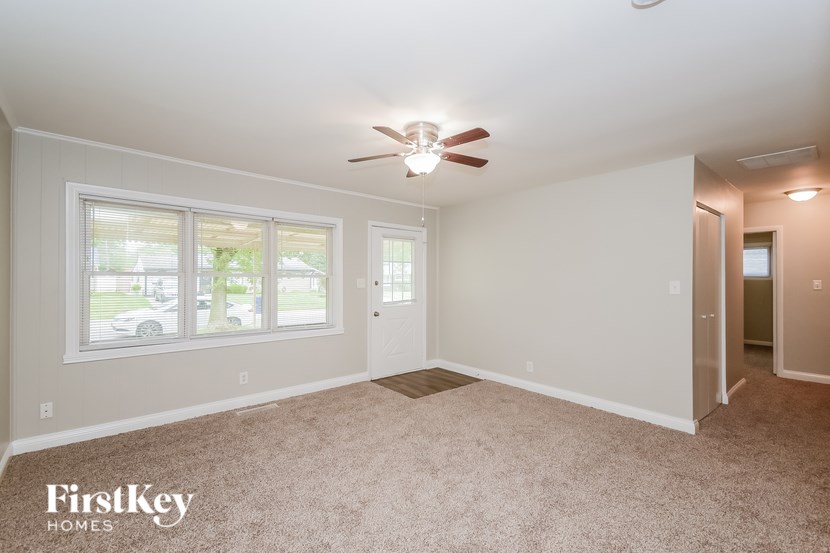 A spacious room with a carpeted floor, a ceiling fan, and a door leading to another room.