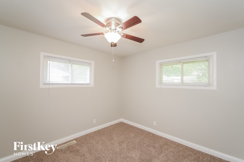 A room with a ceiling fan and two windows.