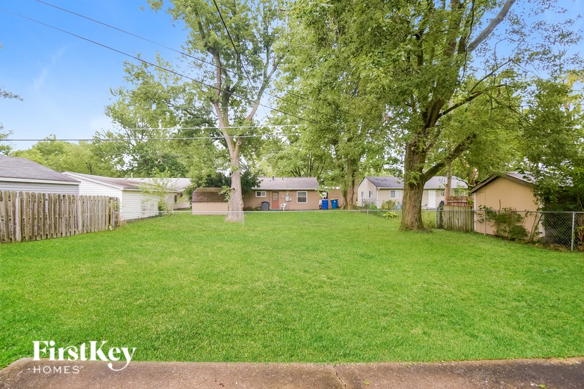 A grassy yard with a fence and houses in the background.