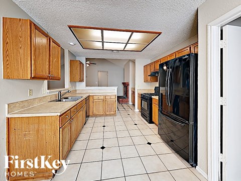 a kitchen with wooden cabinets and tiled floors and a black refrigerator