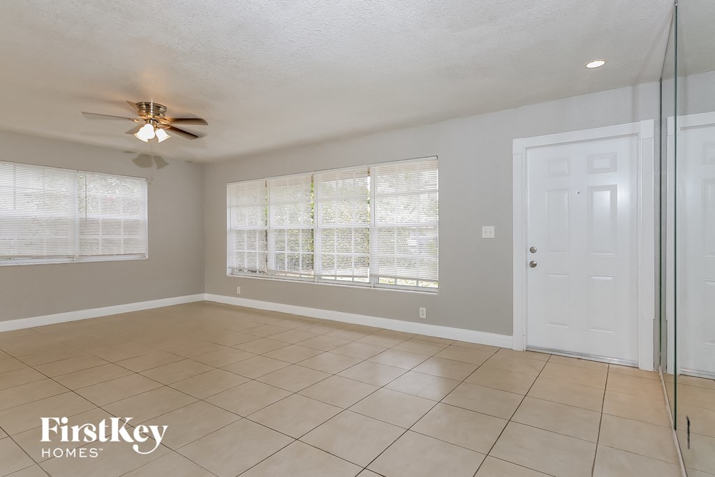 an empty living room with a large window and a ceiling fan