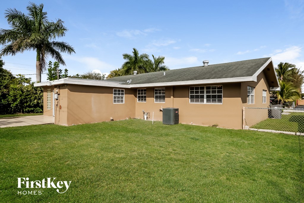 a brown house with a grass yard and palm trees