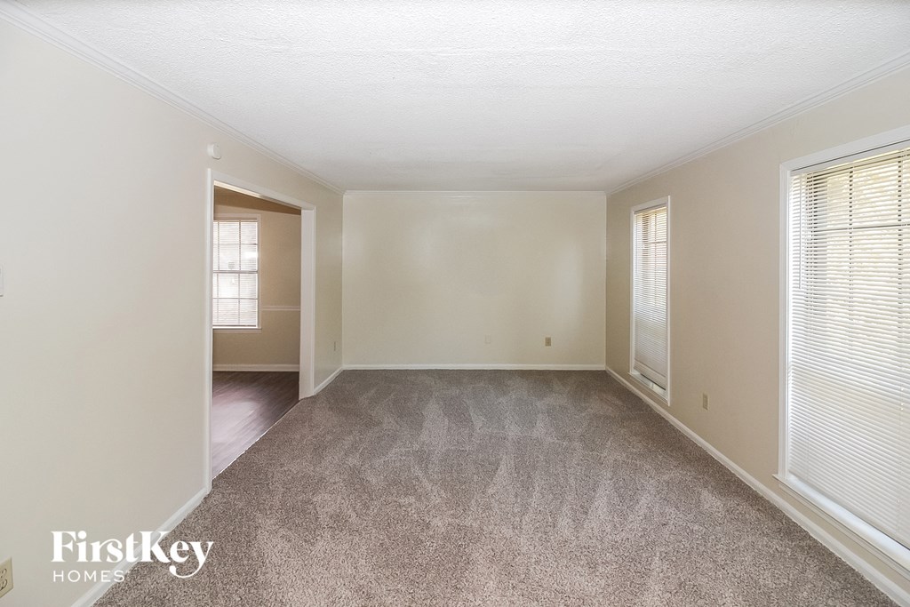 A spacious room with a carpeted floor and a window with blinds.