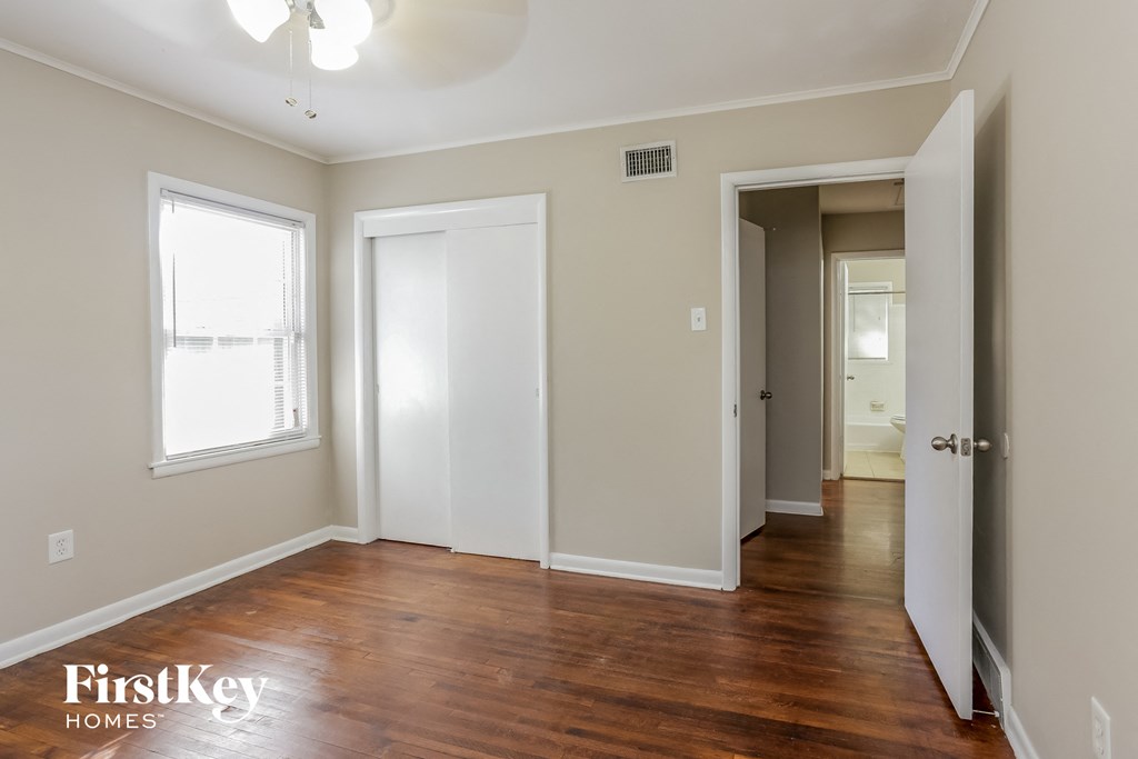 a bedroom with a hardwood floor and a door to a hallway and a closet