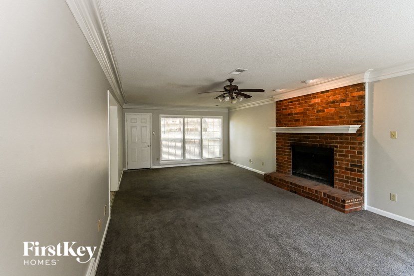 an empty living room with a brick fireplace and a ceiling fan