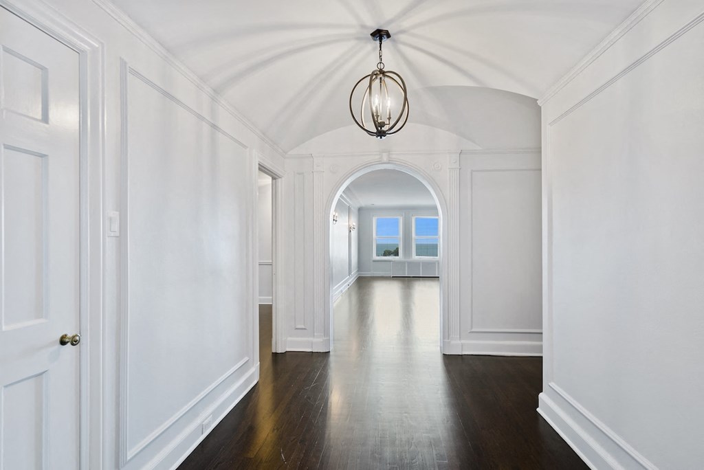 a long hallway with white walls and wood floors and an arched doorway