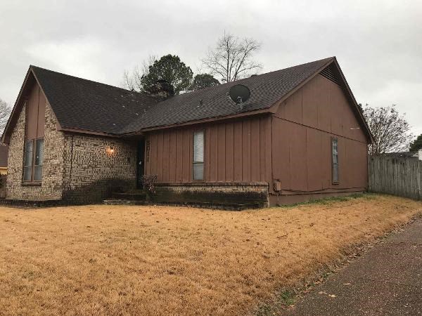 A brown house with a stone wall and a brown fence.