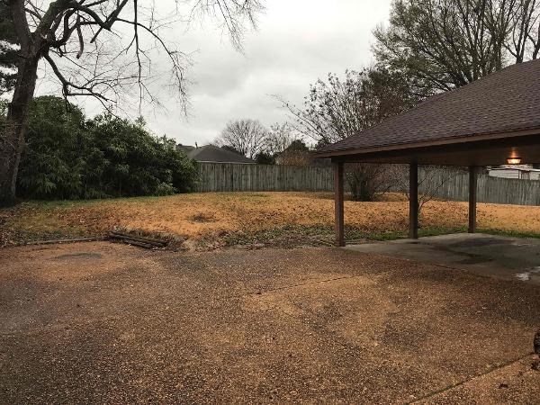 A backyard with a brown roofed gazebo and a fence.