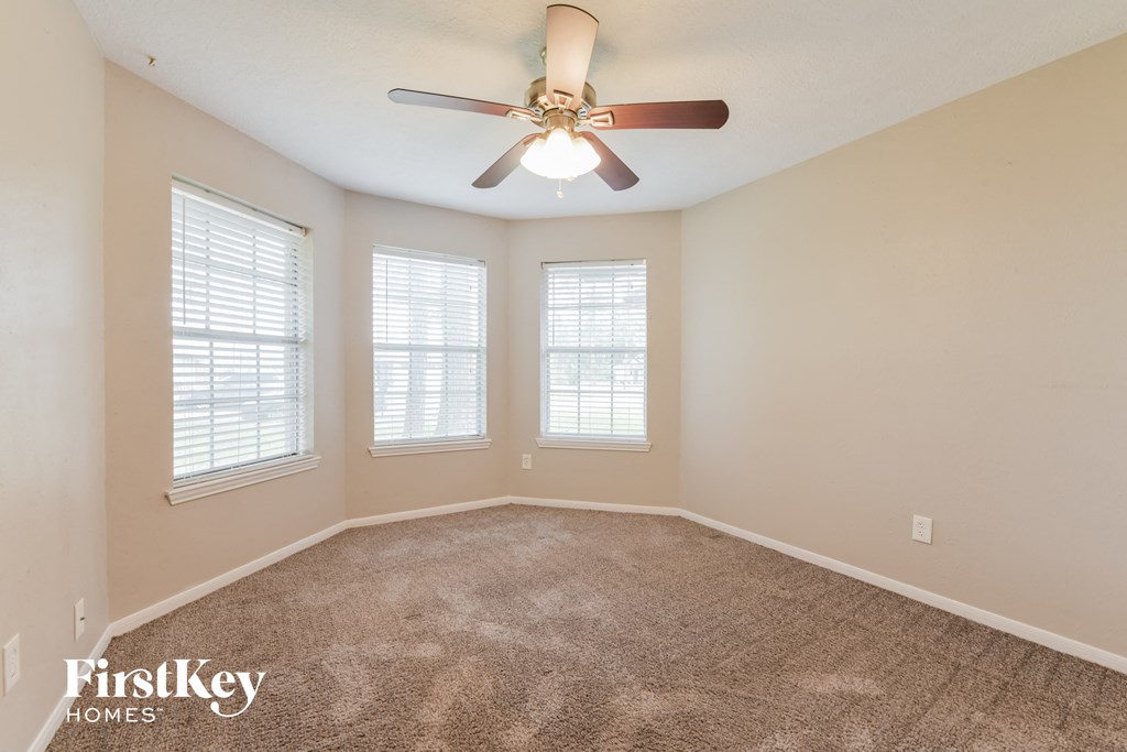 an empty room with a ceiling fan and three windows
