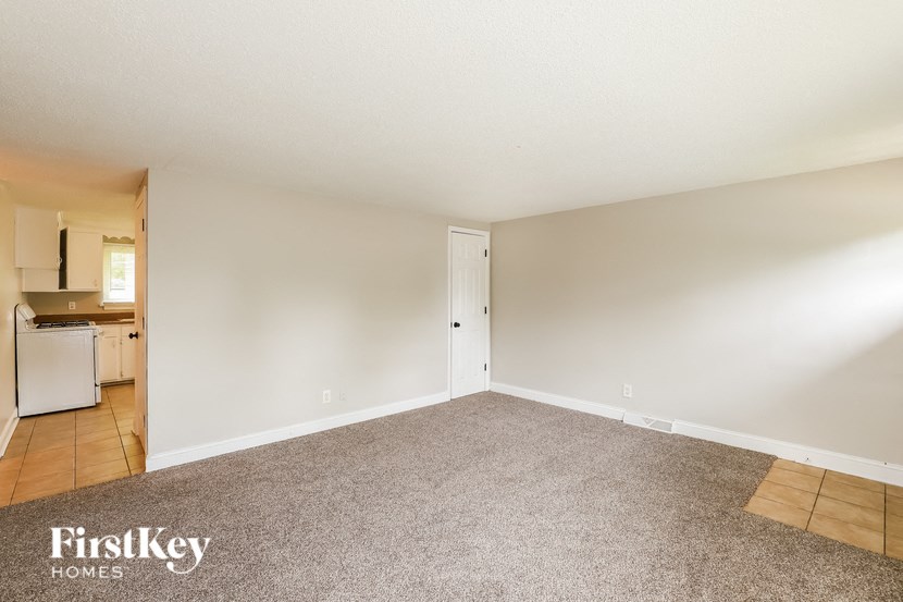 an empty living room with carpet and a kitchen