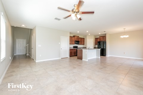 A spacious living room with a ceiling fan and lighting fixtures.