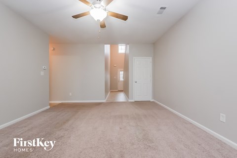 a spacious living room with white carpet and a ceiling fan
