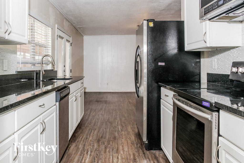 a kitchen with white cabinets and black counter tops and a black refrigerator