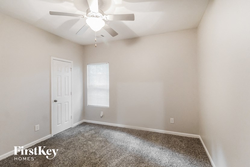 the spacious living room with white walls and a ceiling fan