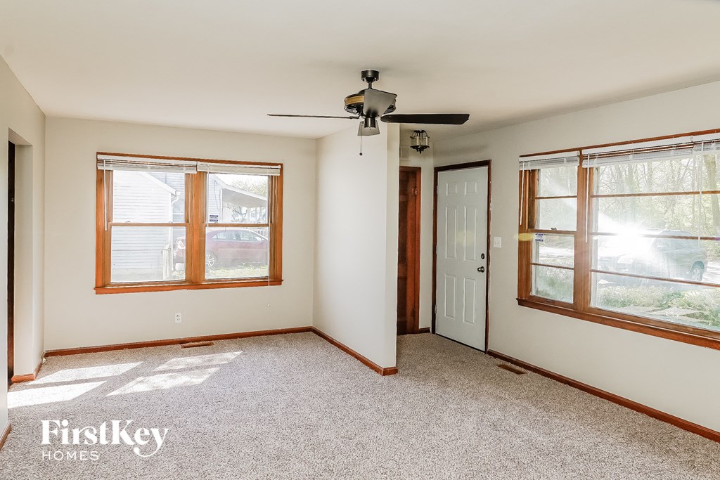 A room with a carpet floor, a ceiling fan, and two windows.
