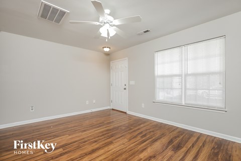 the spacious living room with wood flooring and a ceiling fan