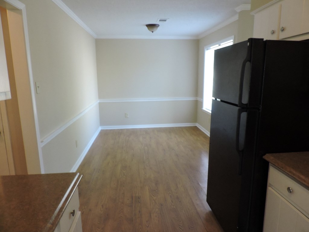 an empty kitchen with a black refrigerator and wooden floors