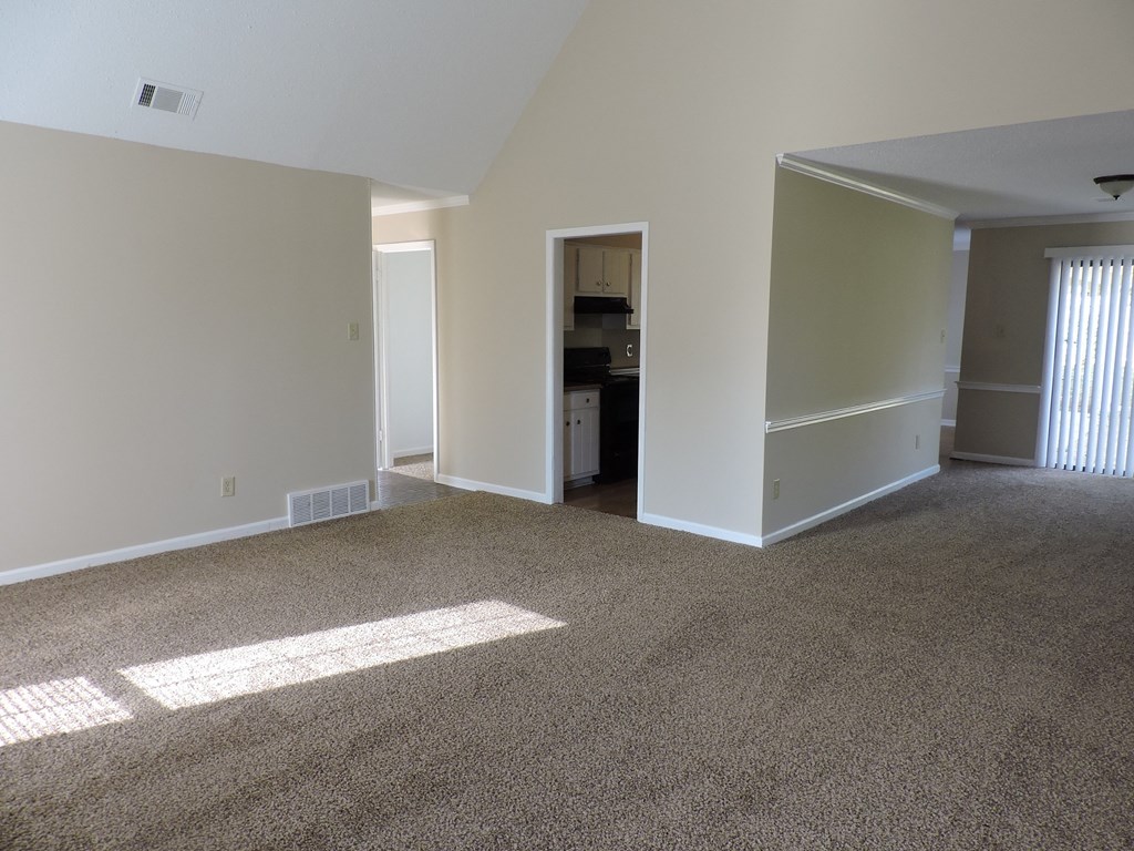 an empty living room with carpet and a kitchen