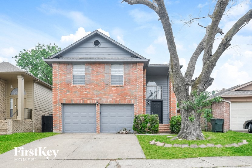A brick house with a grey roof and a tree in front.