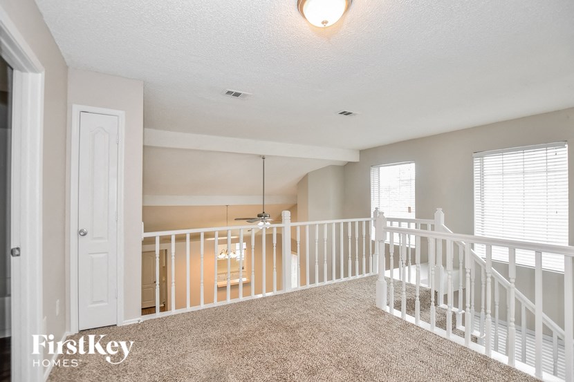 A spacious living room with a carpeted floor and white railings.