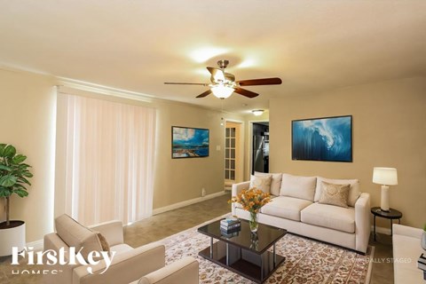 A living room with a white couch, a coffee table, a ceiling fan, and two paintings on the wall.
