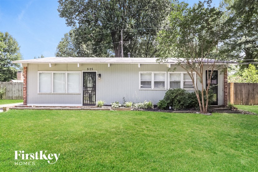 a small white house with a lawn and trees