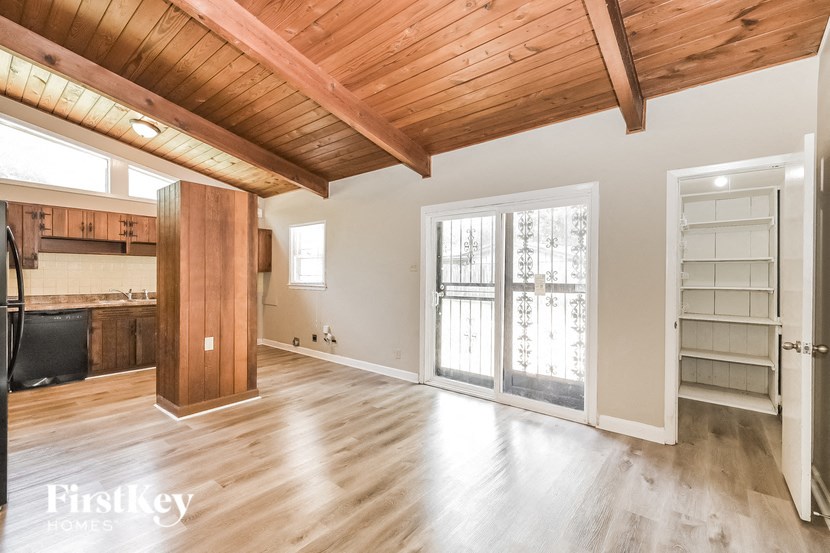 an empty living room with wood floors and a door to a kitchen