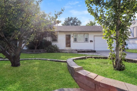 the front of a white house with a yard and a retaining wall