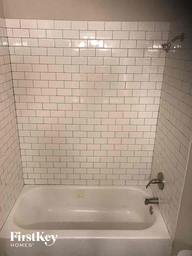 a white tiled bathroom with a tub and a toilet