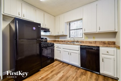 A black refrigerator is in a kitchen with white cabinets.