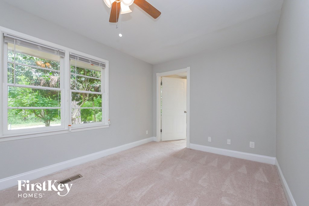 A room with a ceiling fan and a window overlooking a tree.