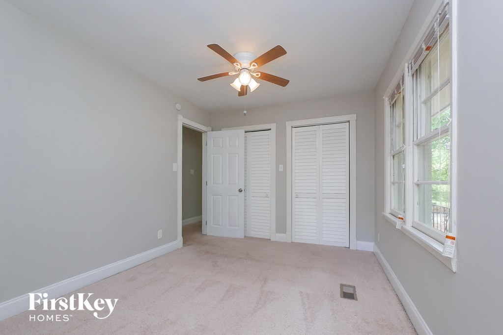 A room with a ceiling fan and a window with white shutters.