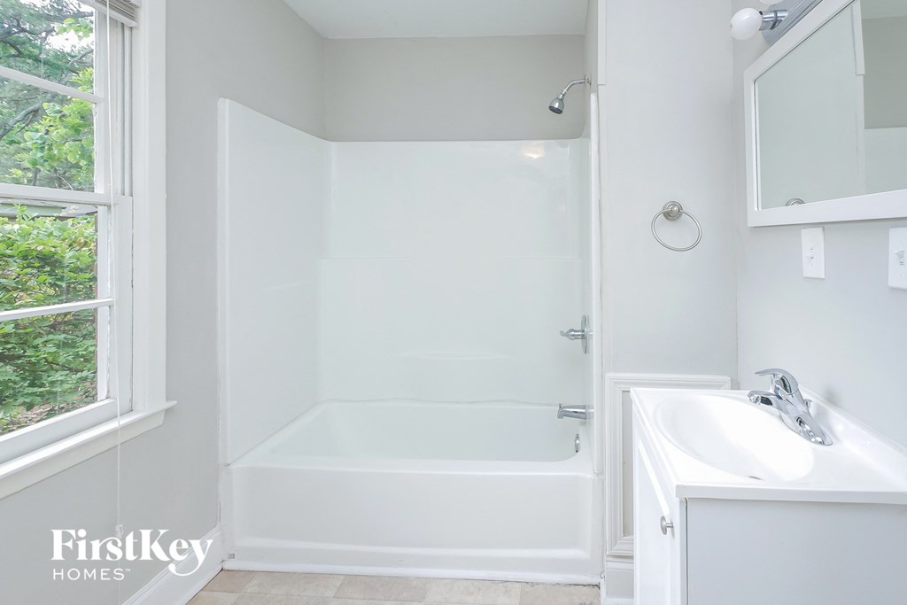 A white bathroom with a tub, sink and mirror.