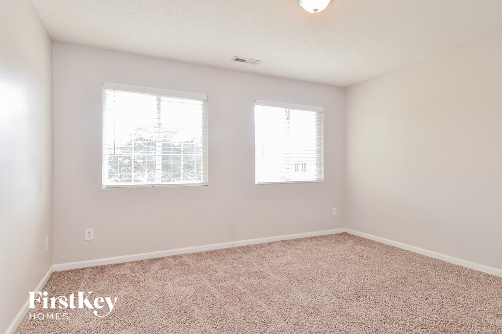 a spacious bedroom with carpet and two windows