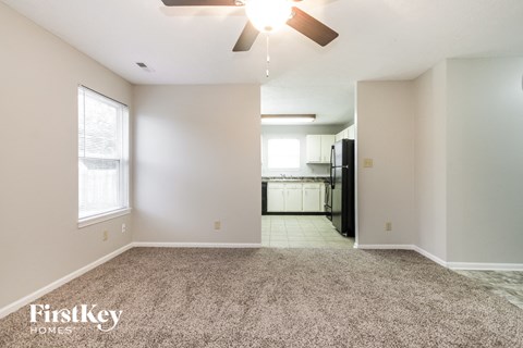 an empty living room with a ceiling fan and a kitchen