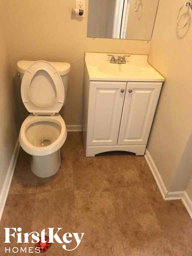 A white toilet is in a bathroom with a white cabinet and a mirror.