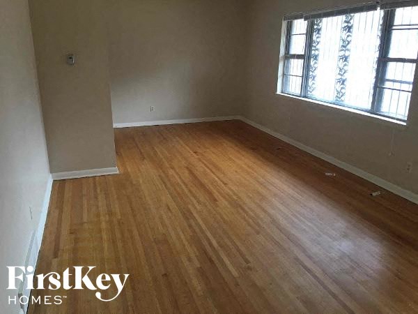 A room with wooden flooring and a window with a view of a building.