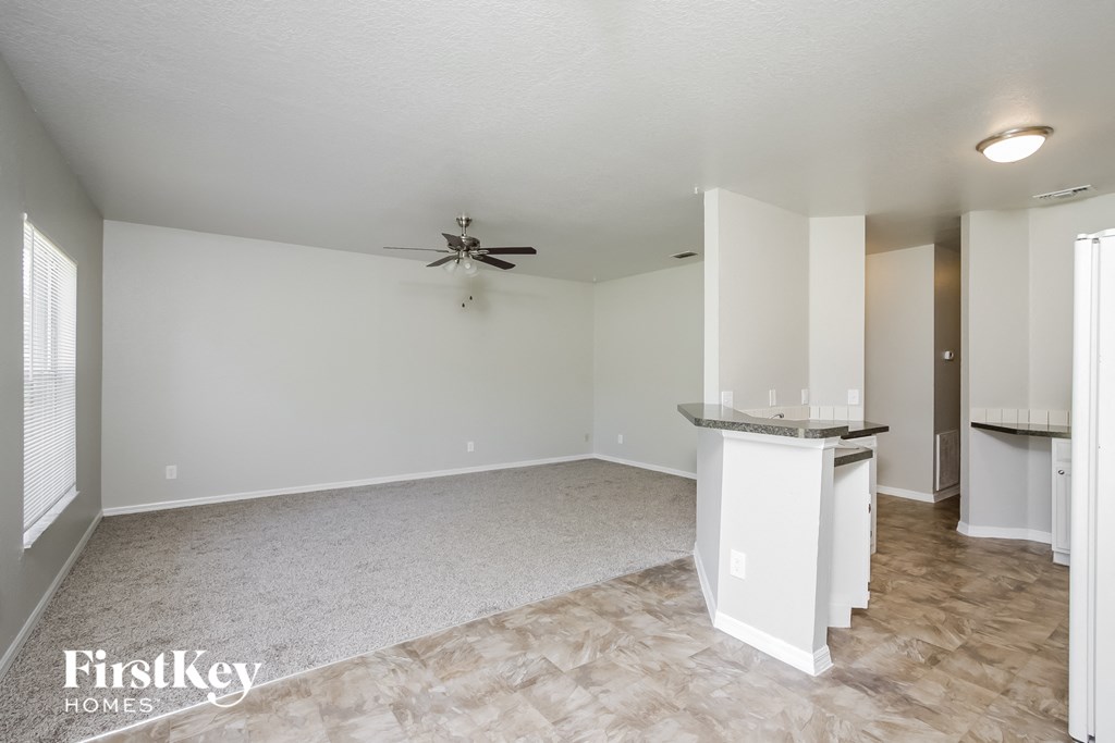 an empty living room with a kitchen and a ceiling fan