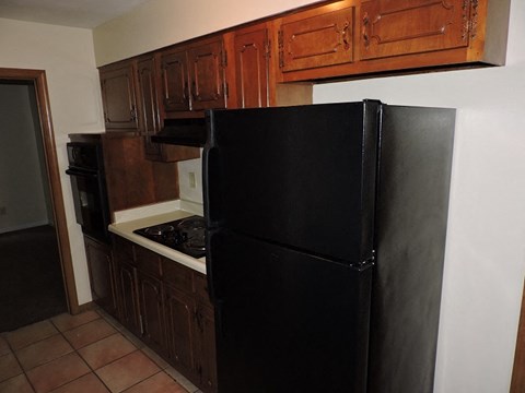 A black refrigerator in a kitchen with brown cabinets.