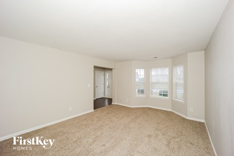 a spacious living room with carpet and a door to a hallway
